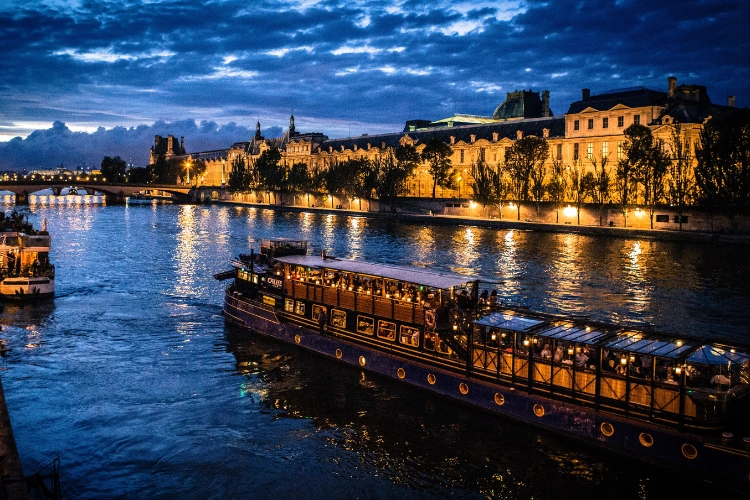 Opplyst båt på Seine i Paris om kvelden, foran Louvre, illustrerer en elegant atmosfære etter en spillsesjon
