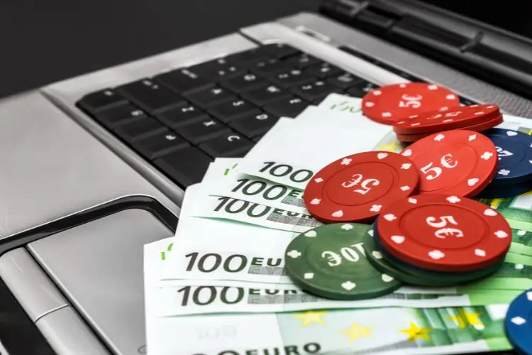 Billets de 100 € et jetons de casino posés sur un clavier d'ordinateur portable